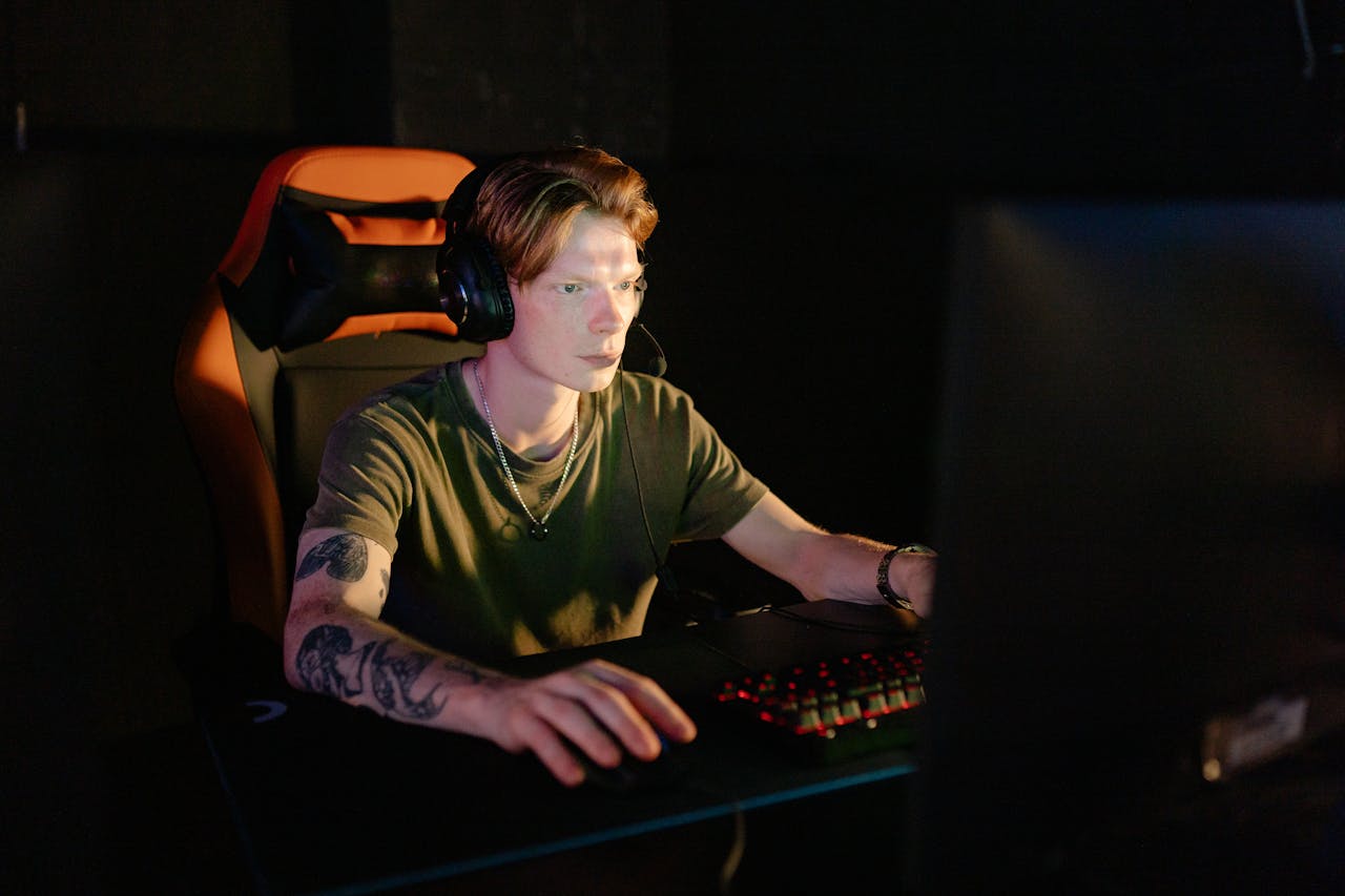 A young man engrossed in a video game, wearing headphones and using a gaming chair.